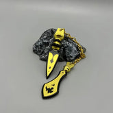 Anime-style zinc alloy weapon keychain with gold and black blades on stone display
