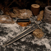 Greatsword of Solitude replica resting on rocks in a snowy setting with dry brown branches and a miniature stone well in the background.