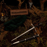 Ranger Sword metal replica unsheathed on moss, surrounded by a green cloak, twisted roots, a mini campfire, and the Evenstar pendant.