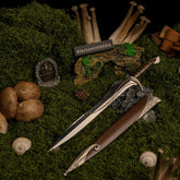 Sting metal replica sword unsheathed on fresh green moss with mini mushrooms, pinecones, and a Hobbit door.