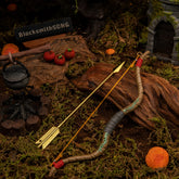 The complete 18cm metal Zelda Wooden Bow prop and golden arrow resting on dark earth amidst a Breath of the Wild campsite diorama, featuring a cooking pot and red Hylian apples.