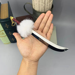 Hand holding 1:6 anime-style zinc alloy mini sword with white fluffy pompom, collectible cosplay display.