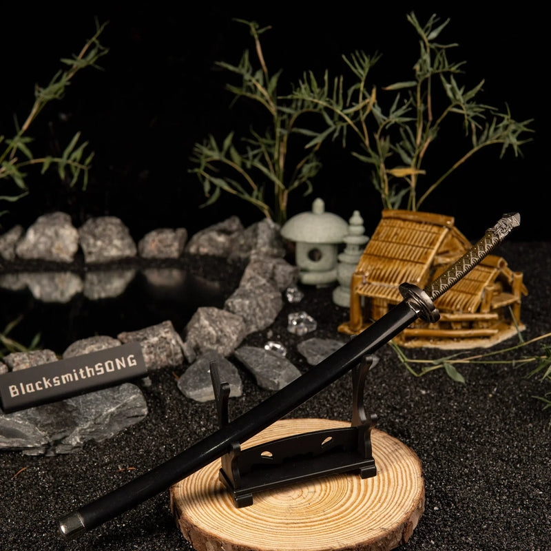 Add a touch of magic to your gaming setup.  This Moonveil Katana metal replica is displayed on a sleek black stand, perfect for a Zen-inspired desk theme. Crafted from zinc alloy, this Elden Ring weapon brings the calm and deadly aesthetic of the Transient Moonlight to your room. - Small display stand