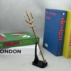 Gold anime-style zinc alloy trident replica on stand, collectible display near colorful books.
