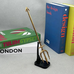 Anime-style gold trident zinc alloy replica on stand, displayed with books, BlacksmithSONG collectible.