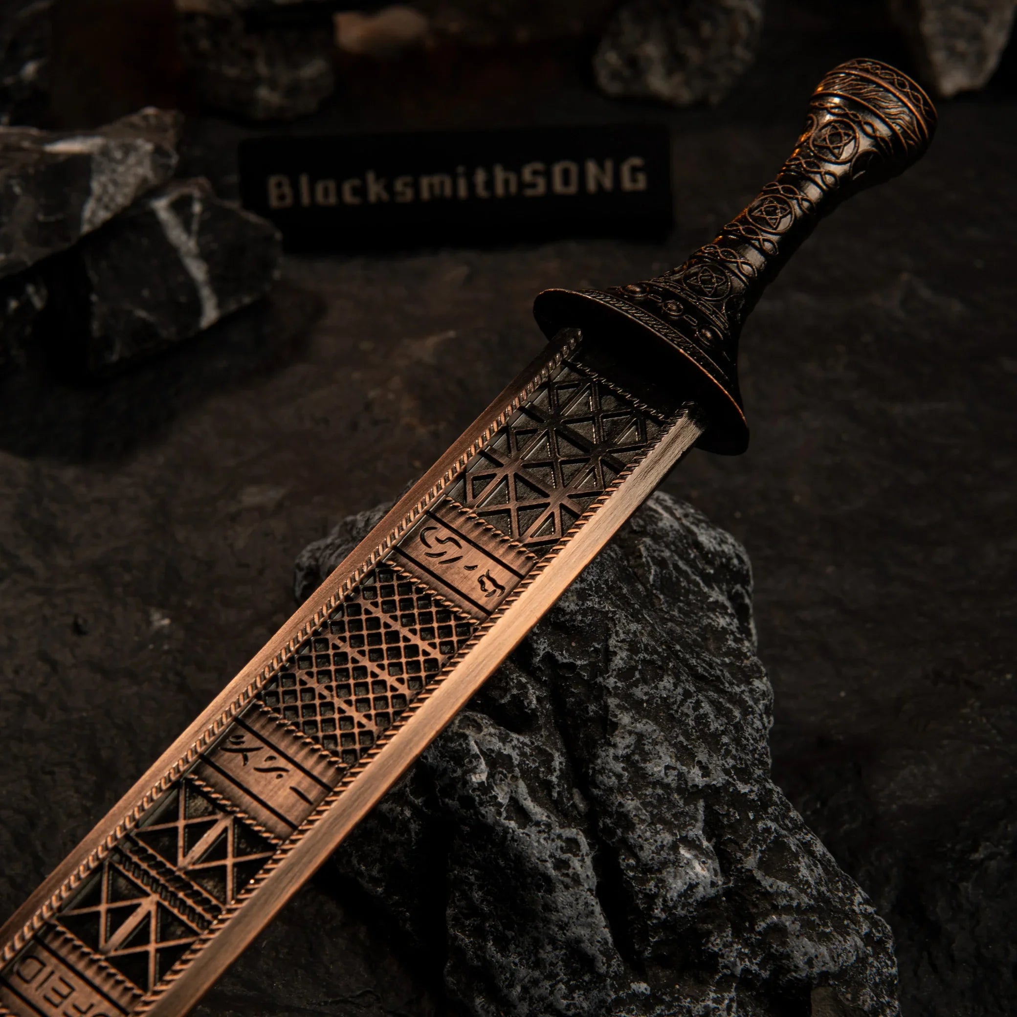 A macro close-up shot of the Regalia of Eochaid sword blade resting on a dark rock. The image focuses on the intricate grid-like geometric engravings and runes on the bronze-colored metal surface. The hilt is visible in the background.