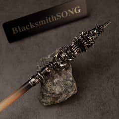 Chitin Staff replica — close-up of the ornate metal head on a stone-gray surface.
