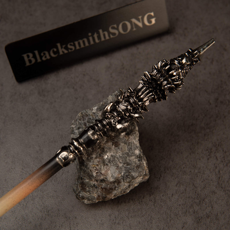 Chitin Staff replica — close-up of the ornate metal head on a stone-gray surface.