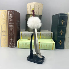 Anime-style zinc alloy sword replica with fluffy white pom, displayed on stand, books in background