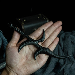 A hand holding the Black Knife dagger replica to show scale against a dark background with fabric.