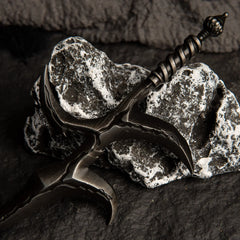 Close-up macro shot of the Black Knife metal replica, focusing on the dark, uneven, wave-like texture of the blade and hilt.