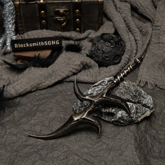 Black Knife metal replica resting on rocks. Background features black feathers, grey fabric, and a moon-like spherical prop.