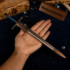 A hand holding the Carian Knight's Sword replica to show scale against a background of vintage books.
