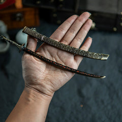 A hand holding the unsheathed Meteoric Ore Blade miniature to show scale and blade detail.