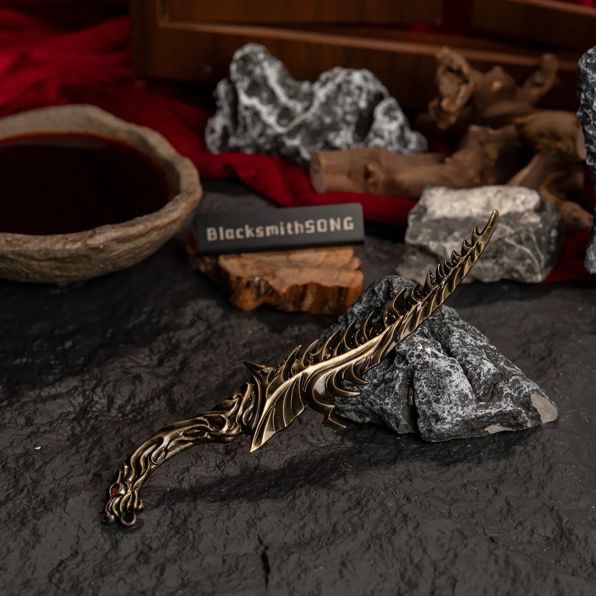 High-angle view of the Reduvia dagger replica on a dark textured surface with red cloth in the background.
