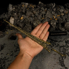 A hand holding the 30cm Dragon King's Cragblade metal replica to show its large scale, against a background of grey sand and rocks.
