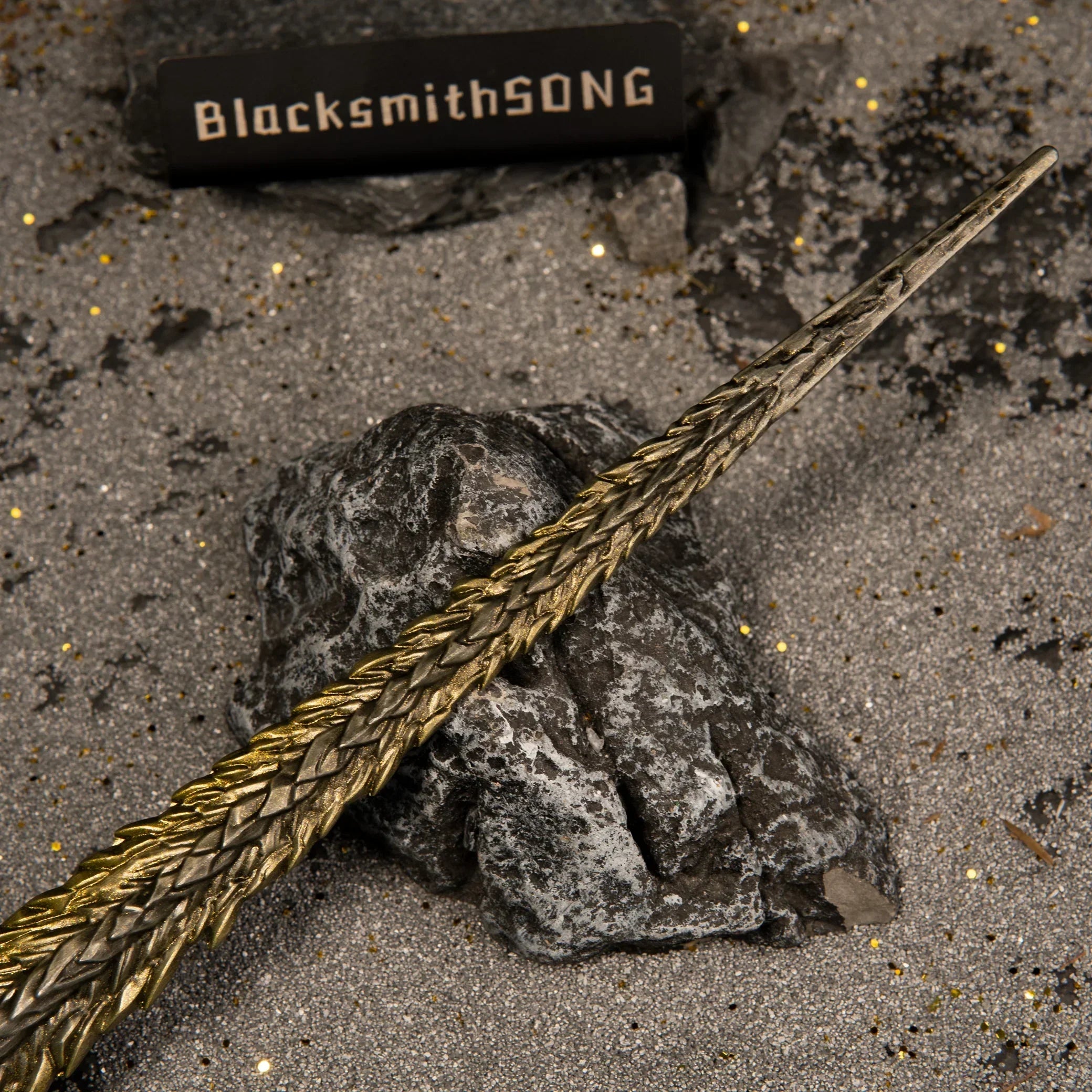 Close-up shot of the textured gold blade of the Dragon King's Cragblade replica resting on a dark grey rock.