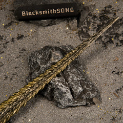 Close-up shot of the textured gold blade of the Dragon King's Cragblade replica resting on a dark grey rock.