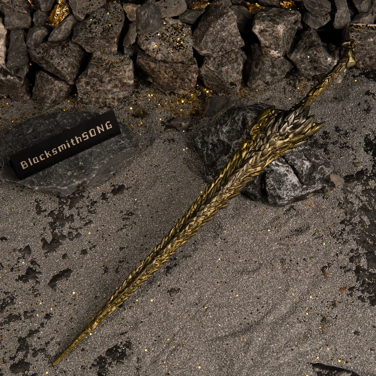 High-angle view of the Dragon King's Cragblade lying horizontally on dark, glittery sand and grey rocks.