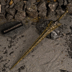 High-angle view of the Dragon King's Cragblade lying horizontally on dark, glittery sand and grey rocks.