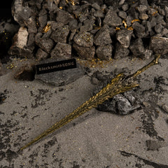 Dragon King's Cragblade replica resting on grey rocks. The background features dark sand, gold flakes, and small stones suspended in the air.