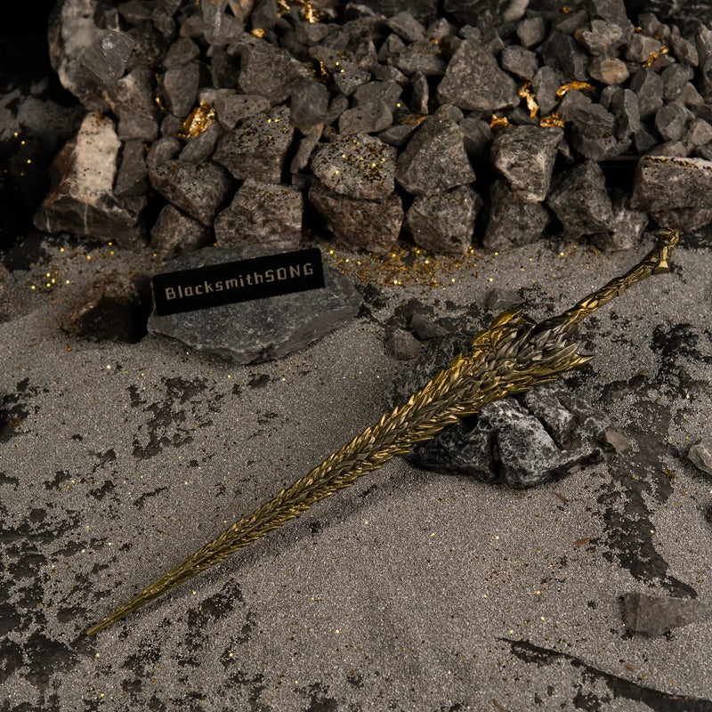Dragon King's Cragblade replica resting on grey rocks. The background features dark sand, gold flakes, and small stones suspended in the air.