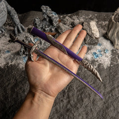 A hand holding the unsheathed Dragonscale Blade replica to show scale against a dark background with snow and blue crystals.