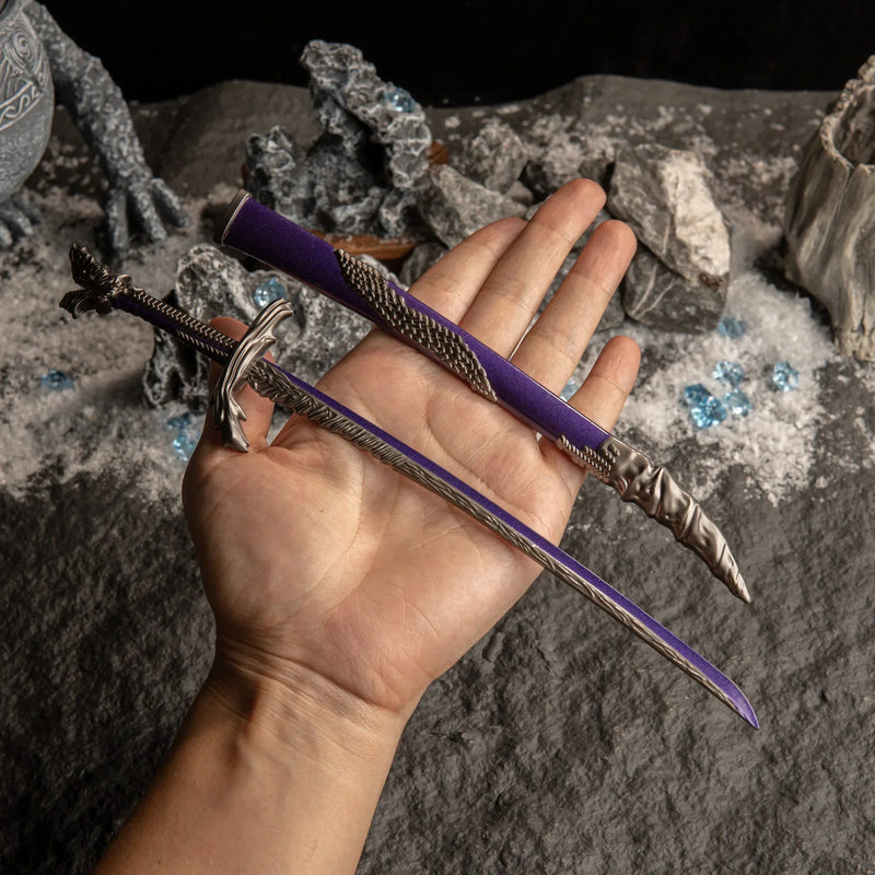 A hand holding the unsheathed Dragonscale Blade replica to show scale against a dark background with snow and blue crystals.
