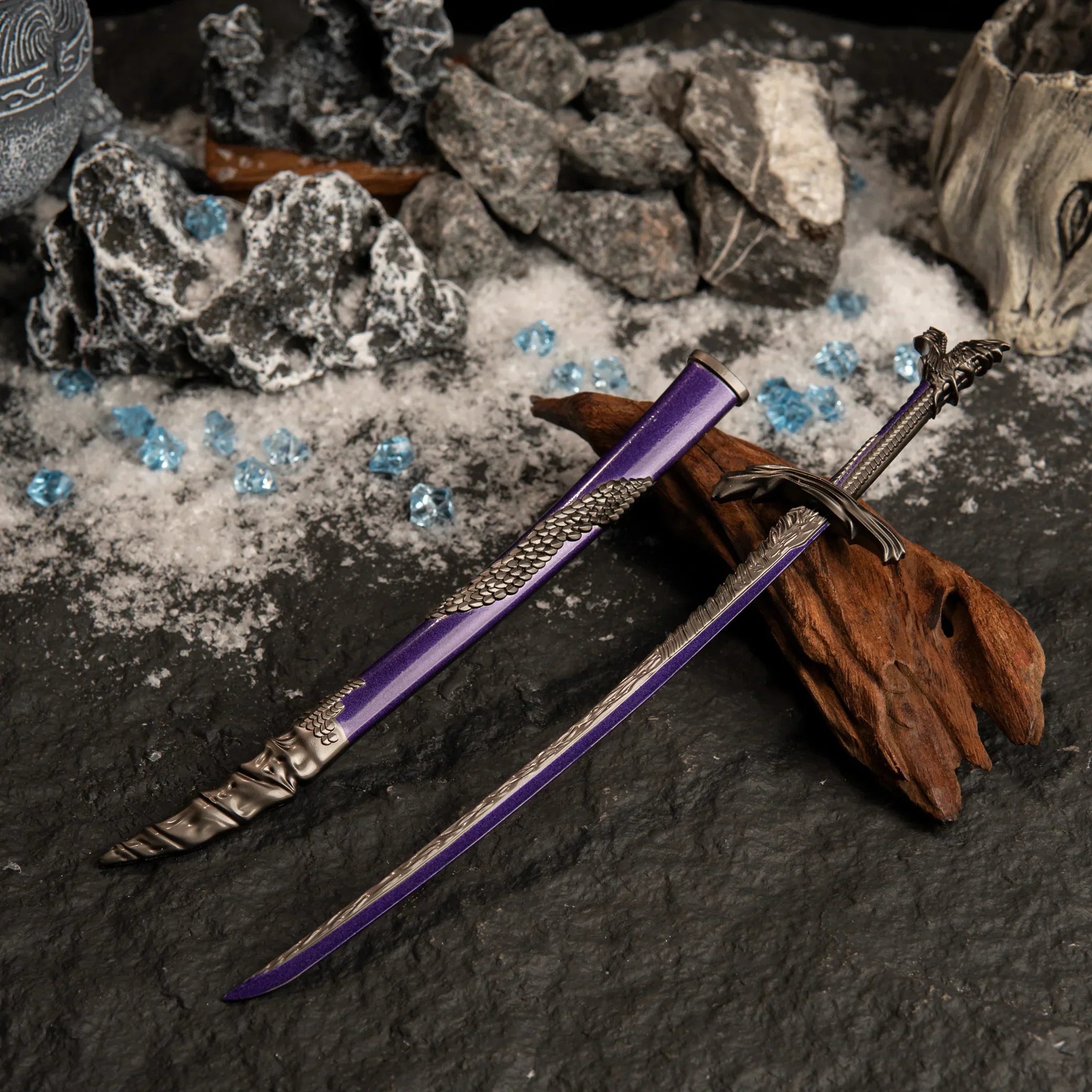 Dragonscale Blade replica resting on dark wood, surrounded by artificial snow, grey rocks, and scattered blue crystal props.
