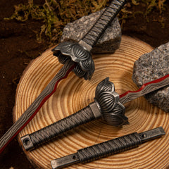 Close-up of the Eleonora's Poleblade metal miniature's lotus-bud guard and crimson red wave patterns on a wood slice.