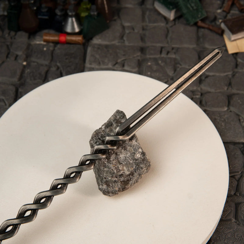 Close-up of the pommel and dark-steel finish of the Fire Knight's Greatsword replica resting against a dark rock.