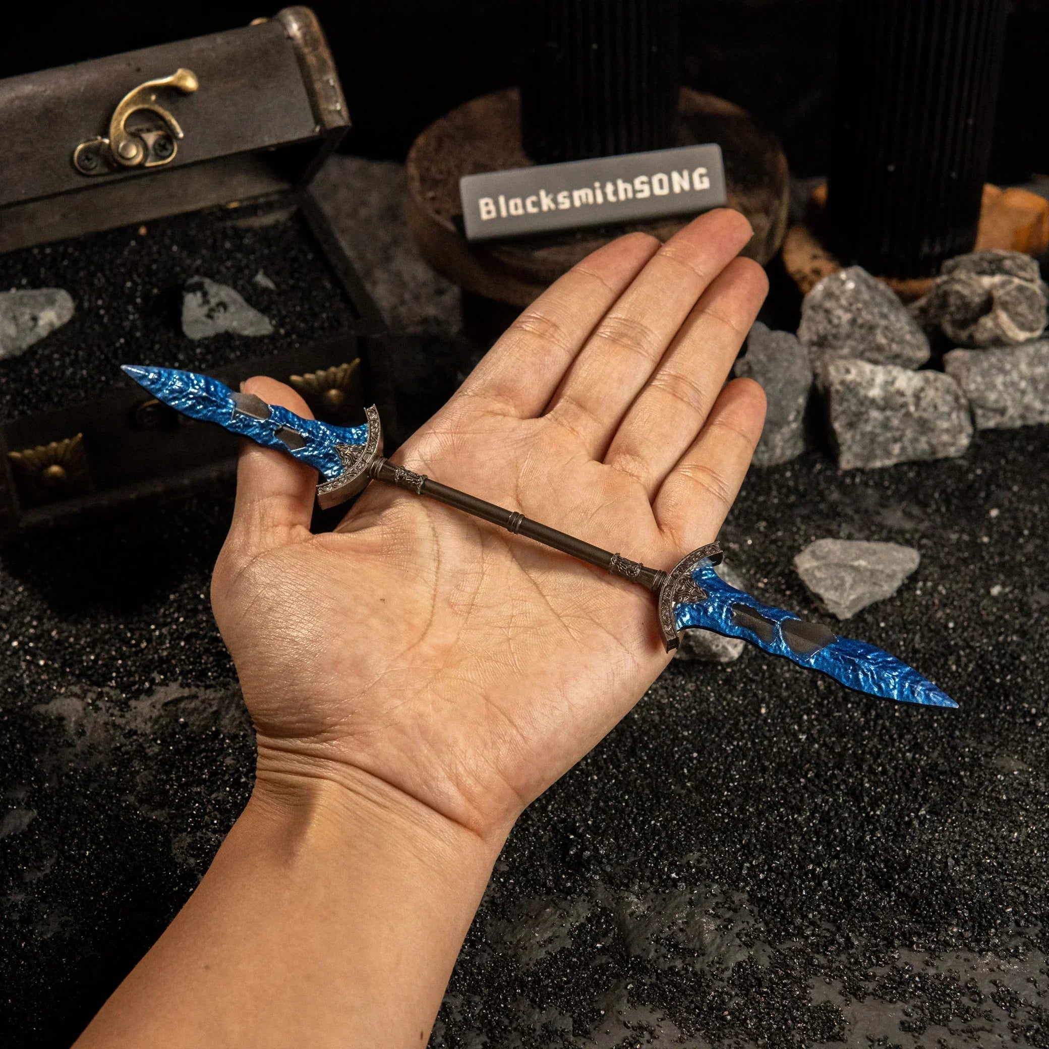 A hand holding the Gargoyle's Black Blades replica to show scale against a background of black sand and rocks.