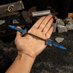 A hand holding the Gargoyle's Black Blades replica to show scale against a background of black sand and rocks.