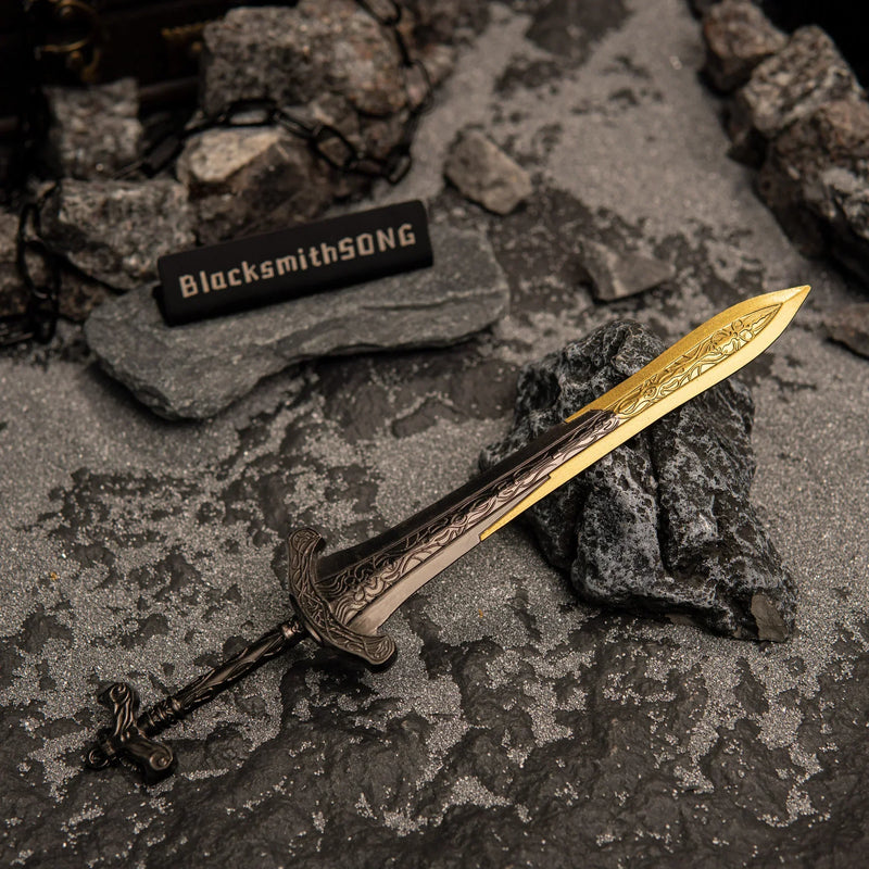 Angled overhead view of the Gargoyle's Greatsword miniature lying on grey sand in a catacomb diorama setting with rocks and chains.