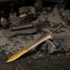 Gargoyle's Greatsword metal replica resting diagonally on a dark rock, surrounded by grey sand, iron chains, and a miniature treasure chest.