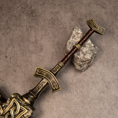 Giant-Crusher replica — grip and pommel resting beside a grey stone.