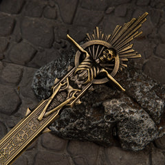 Golden Epitaph replica — rayed sunburst and skull at the blade's end, close-up on stone.