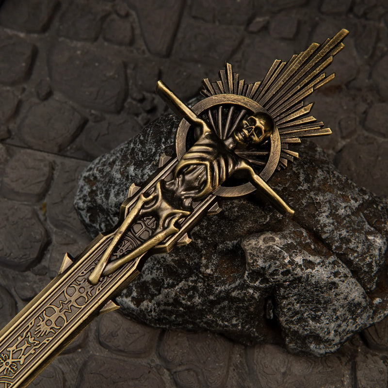 Golden Epitaph replica — rayed sunburst and skull at the blade's end, close-up on stone.