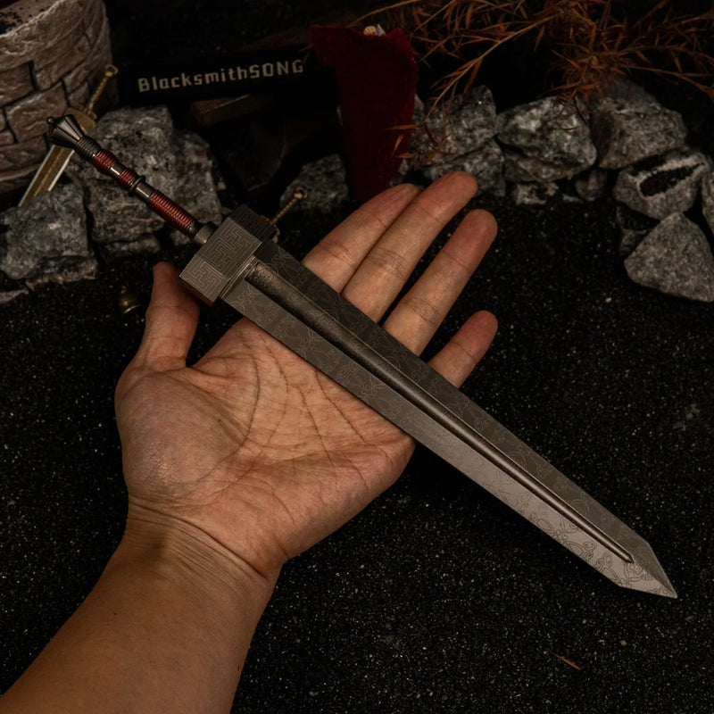 A hand holding the massive 30cm Greatsword metal replica to show its scale, highlighting the wide grey blade and red-wrapped handle against a dark background.
