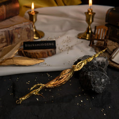 Greatsword of Damnation replica resting on dark rocks. The background features lit candles, vintage books, and gold feathers.