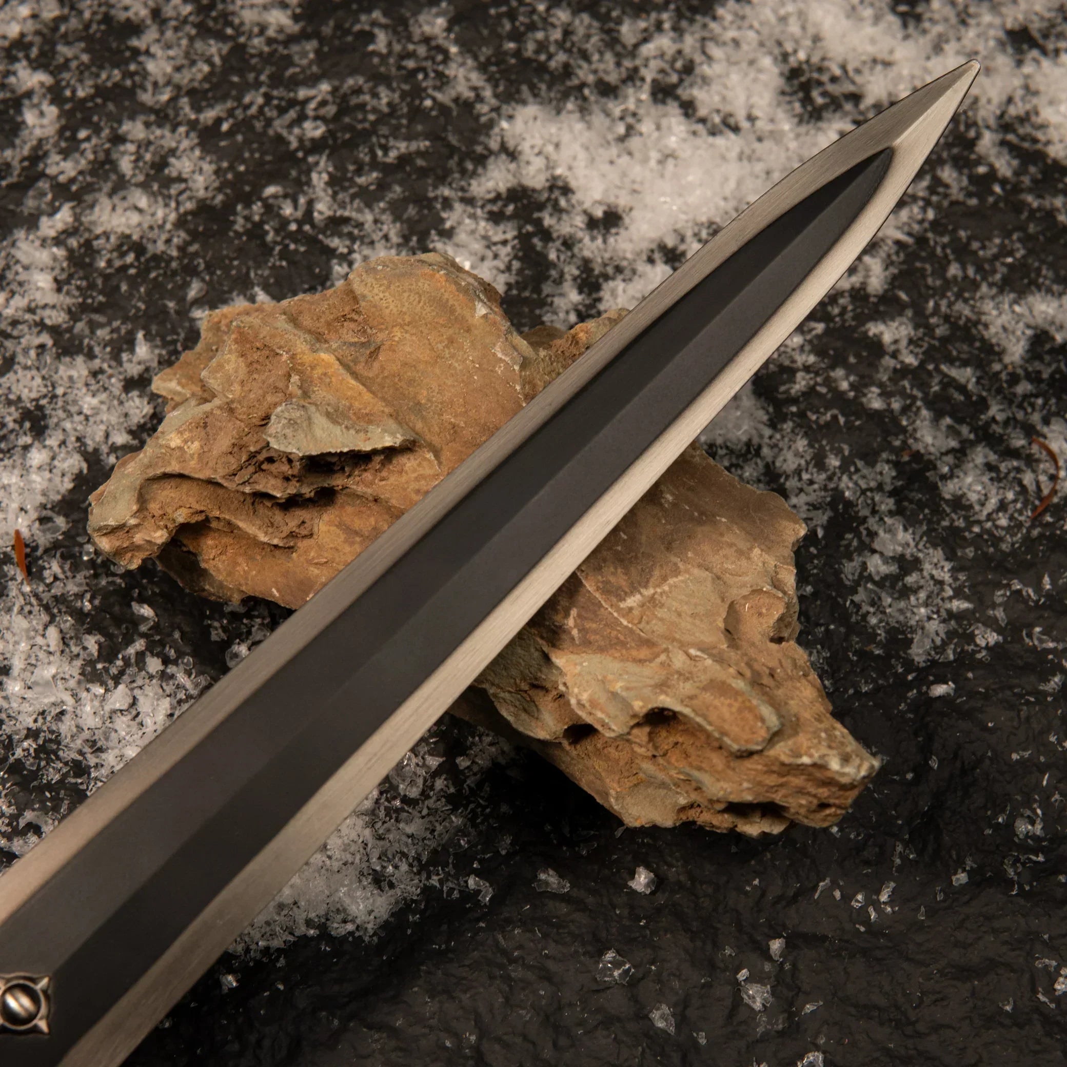 Macro shot of the Greatsword of Solitude blade resting on a rock, highlighting the smooth, dark grey matte finish and silver edges.