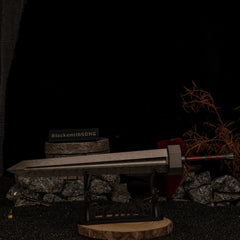 Angled shot of the massive Greatsword replica on a large horizontal display stand, set against a dark background with scattered miniature bells and swords.