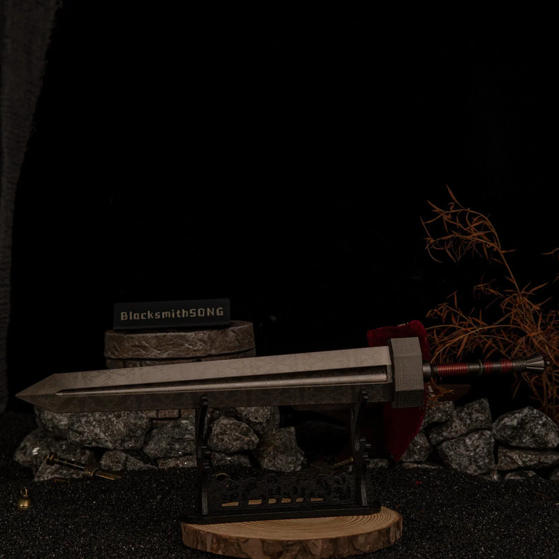 Angled shot of the massive Greatsword replica on a large horizontal display stand, set against a dark background with scattered miniature bells and swords.
