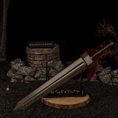 Greatsword 30cm metal replica displayed horizontally on a large black decorative stand over a circular wooden base in a dark ruins setting.