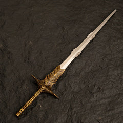 Solid metal replica of Leda's Sword from Elden Ring featuring an intricate gold handle, isolated on a textured black background.