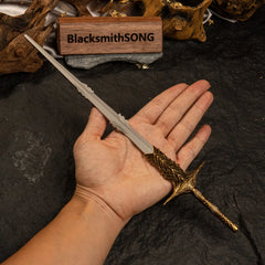 A hand holding the 30cm Leda's Sword metal replica to show its scale and slender design against a dark rock background.