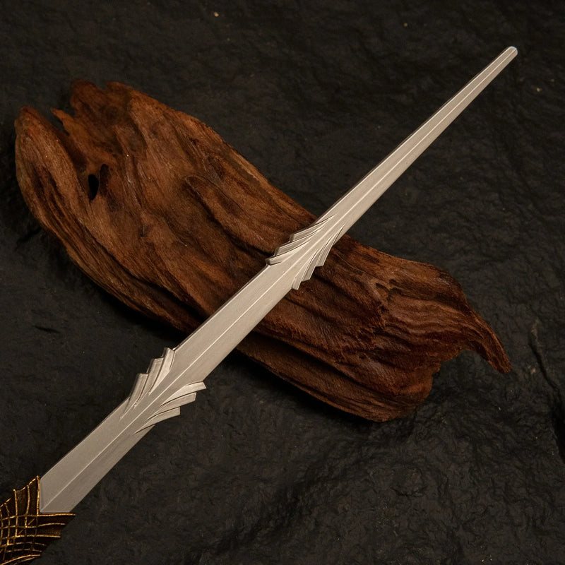 Detailed view of the Leda's Sword metal miniature's golden handle resting on pieces of dark, twisted driftwood.