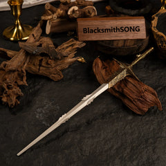 Leda's Sword metal replica displayed on dark slate and driftwood, accompanied by a golden candlestick, scattered gold flakes, and a BlacksmithSONG wooden sign.