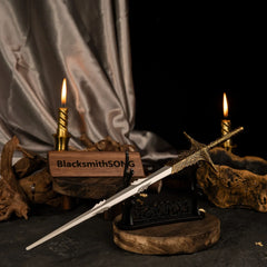 Leda's Sword metal replica displayed horizontally on a large black stand with dark silk fabric and lit candles in the background.