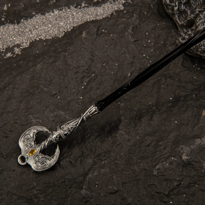 Detailed view of the ornate silver pommel of the Loretta's War Sickle miniature, featuring wing-like metal carvings and a yellow gem accent.